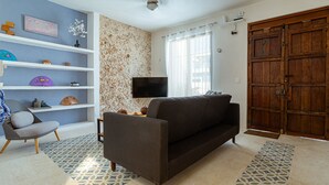 Ein Wohnzimmer mit einer Couch, einem Sessel, einem Fernseher und einer Holztür.
