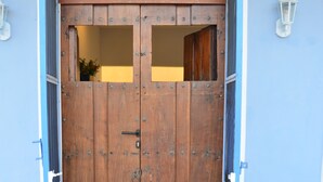 Eine hölzerne Doppeltür mit kleinem Fenster, in eine blaue Wand eingelassen, mit einer weißen Leuchte.