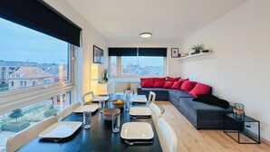 A modern living room with a dining area, large windows, and a view of the city. - Nice apartment in Oostende with Wi-Fi (Oostende)