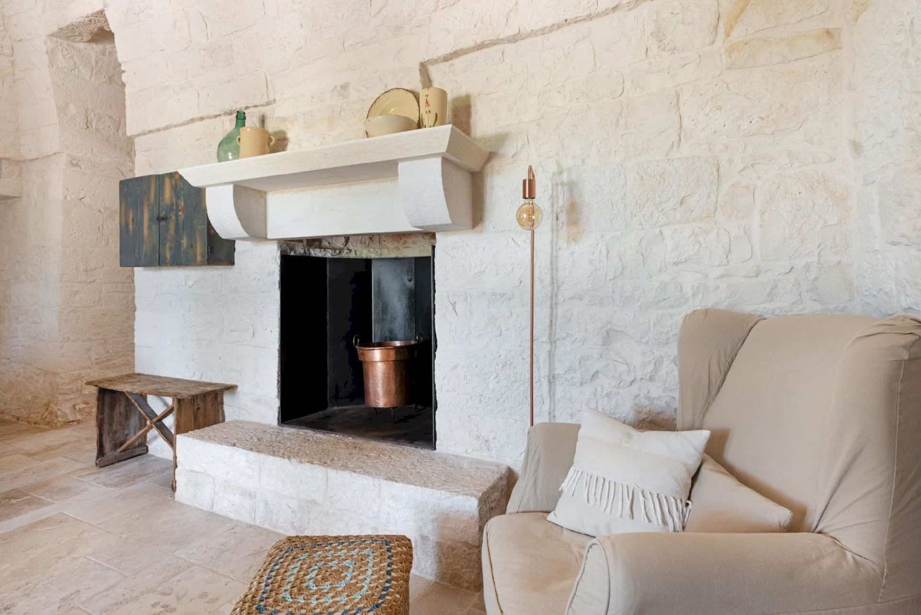 A cozy room with a stone fireplace, a cushioned armchair, and a small wooden table.