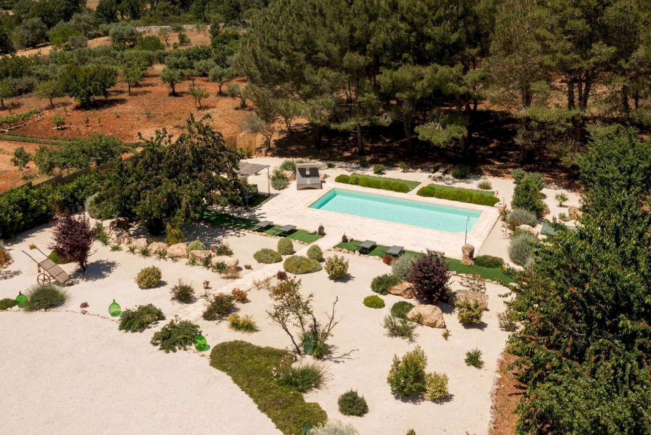 Vue aérienne d’une propriété dotée d’une piscine, entourée de jardins aménagés et d’arbres.
