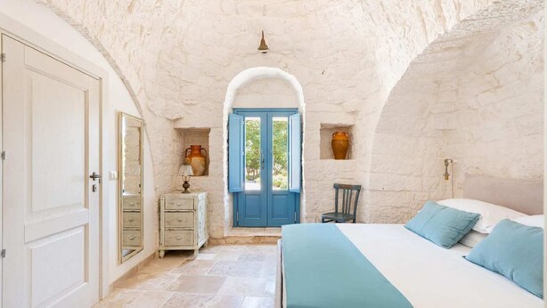 A bedroom with a large bed, a dresser, and a door leading to a balcony.