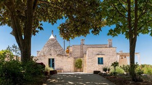 A stone building with a conical roof, a small garden with potted plants, and a clear blue sky.