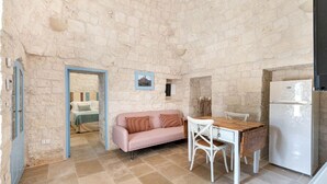 A compact room with a stone wall, a pink sofa, a wooden table, and a white refrigerator. - Trullo Elisa - Trullo with private pool (Monopoli)