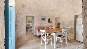 A rustic stone-walled room with a wooden dining table and white chairs, a pink sofa, and a white refrigerator. - Trullo Elisa - Trullo with private pool (Monopoli)