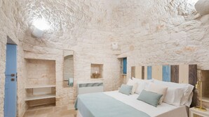 A bedroom with a stone wall, a bed, a nightstand, and a blue door. - Trullo Elisa - Trullo with private pool (Monopoli)
