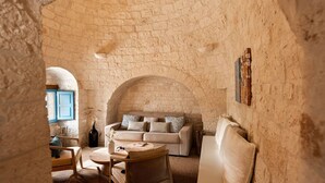 A cozy room with a stone wall, a sofa, a table, and a chair. - Trullo Pia - Trullo with private pool (Monopoli)
