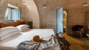 A bedroom with a stone wall, a bed with white linens, a hat, a book, and a wooden bench. - Trullo Pia - Trullo with private pool (Monopoli)