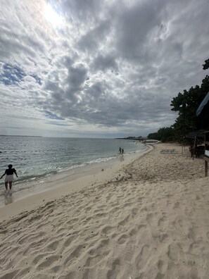 A beach with a sandy shore, a few people walking, and a structure on the right. - HERMOSO APTO DE PLAYA, LA ROMANA (caleta)