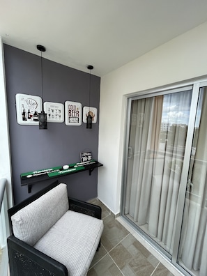 A balcony with a grey wall, a black chair, and a sliding glass door. There are framed signs on the wall and a green sign on a black shelf.