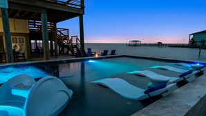 A pool with floating loungers and a deck area with chairs and tables. - Luxury Waterfront Retreat: Pool, Fishing & 5BR, Sleeps 12 (Rockport)