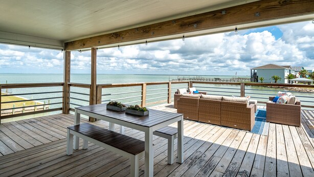 A wooden deck with a white table and benches, overlooking a beach and ocean. - Luxury Waterfront Retreat: Pool, Fishing & 5BR, Sleeps 12 (Rockport)