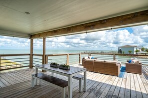 Eine Holzterrasse mit einem weißen Tisch und Bänken, mit Blick auf einen Strand und den Ozean.