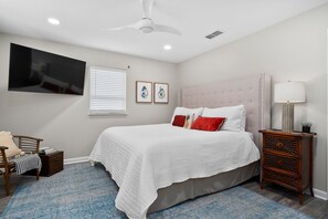 Ein Schlafzimmer mit einem Bett, einem Nachttisch, einem Sessel, einem Deckenventilator und einem an der Wand befestigten Fernseher.