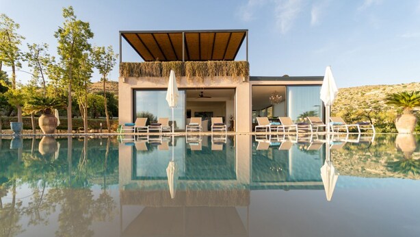 Un edificio moderno con piscina, lettini e una zona coperta vista sul paesaggio.