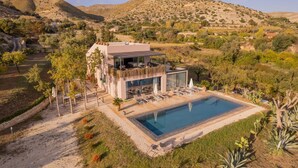 Una villa moderna con piscina, immersa in un giardino curato e circondata da colline.