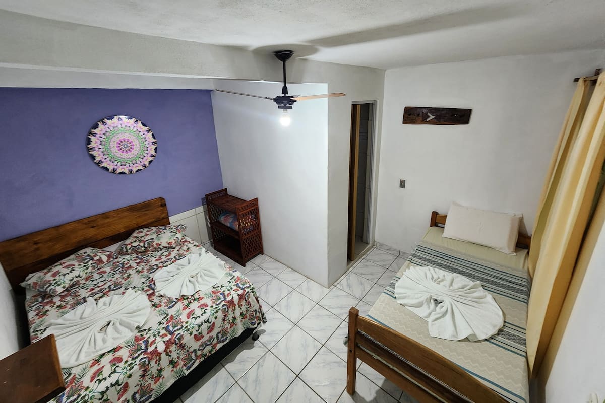 A bedroom with two beds, a ceiling fan, a decorative wall hanging, and a small wooden cabinet.