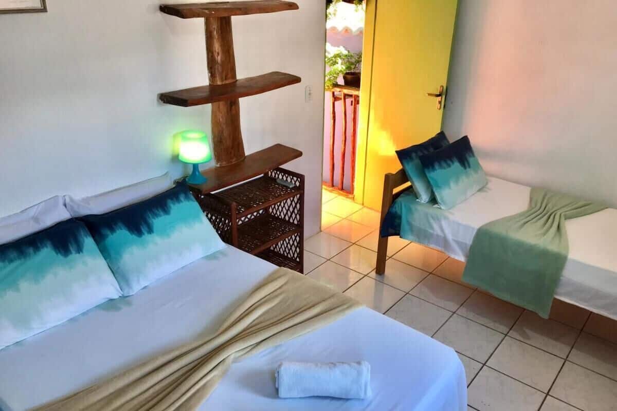 A hotel room with two beds, a wooden shelf, a green lamp, and a view of the outside.