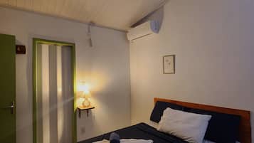 Habitación de hotel con cama, ventilador de techo, aire acondicionado de pared, lámpara de noche y puerta verde.