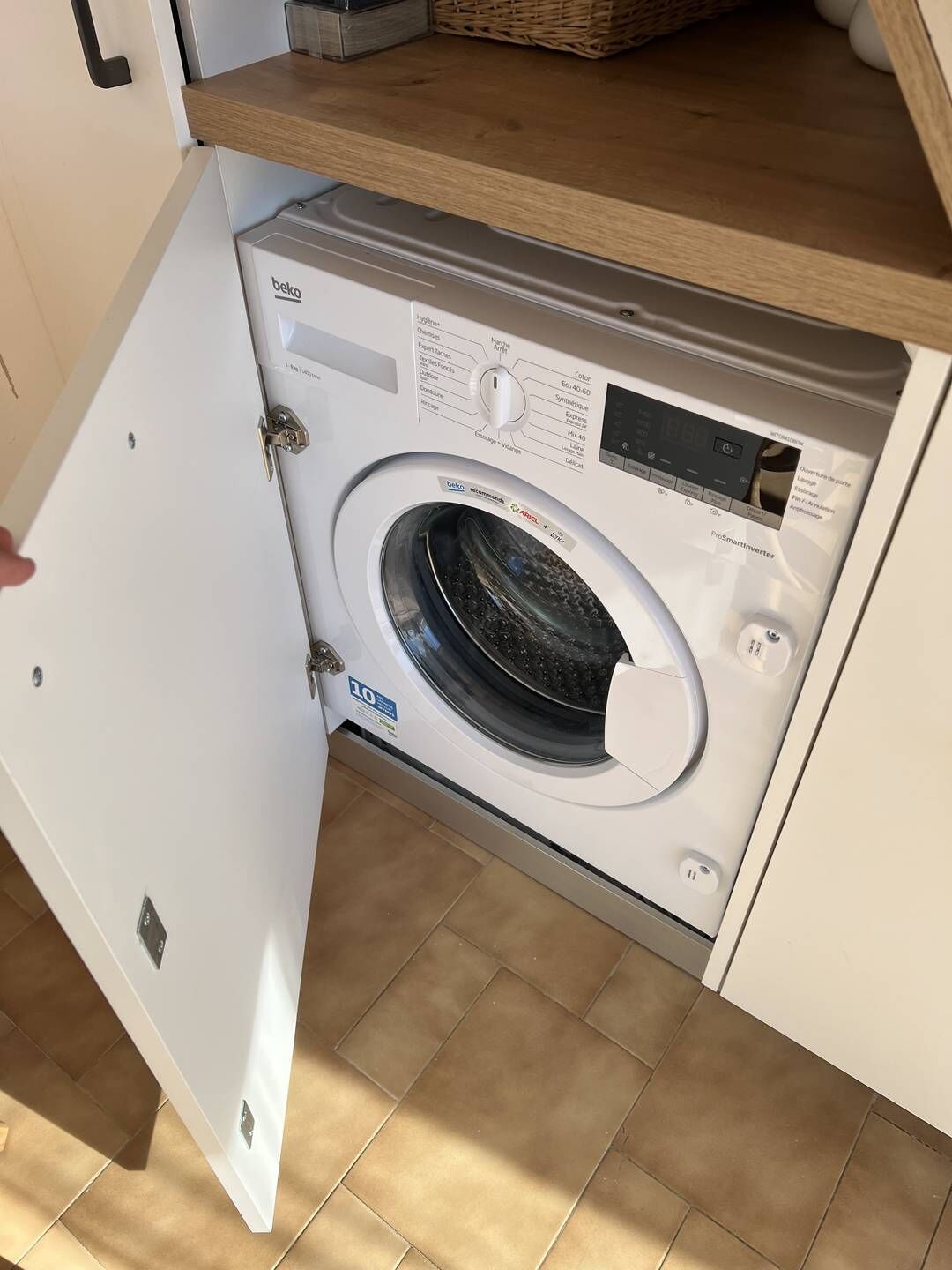 A front-loading washing machine with a control panel, a basket, and a wooden countertop above it.