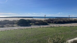 Strandudsigt med klar himmel, sandstrand og græsplæne i forgrunden.