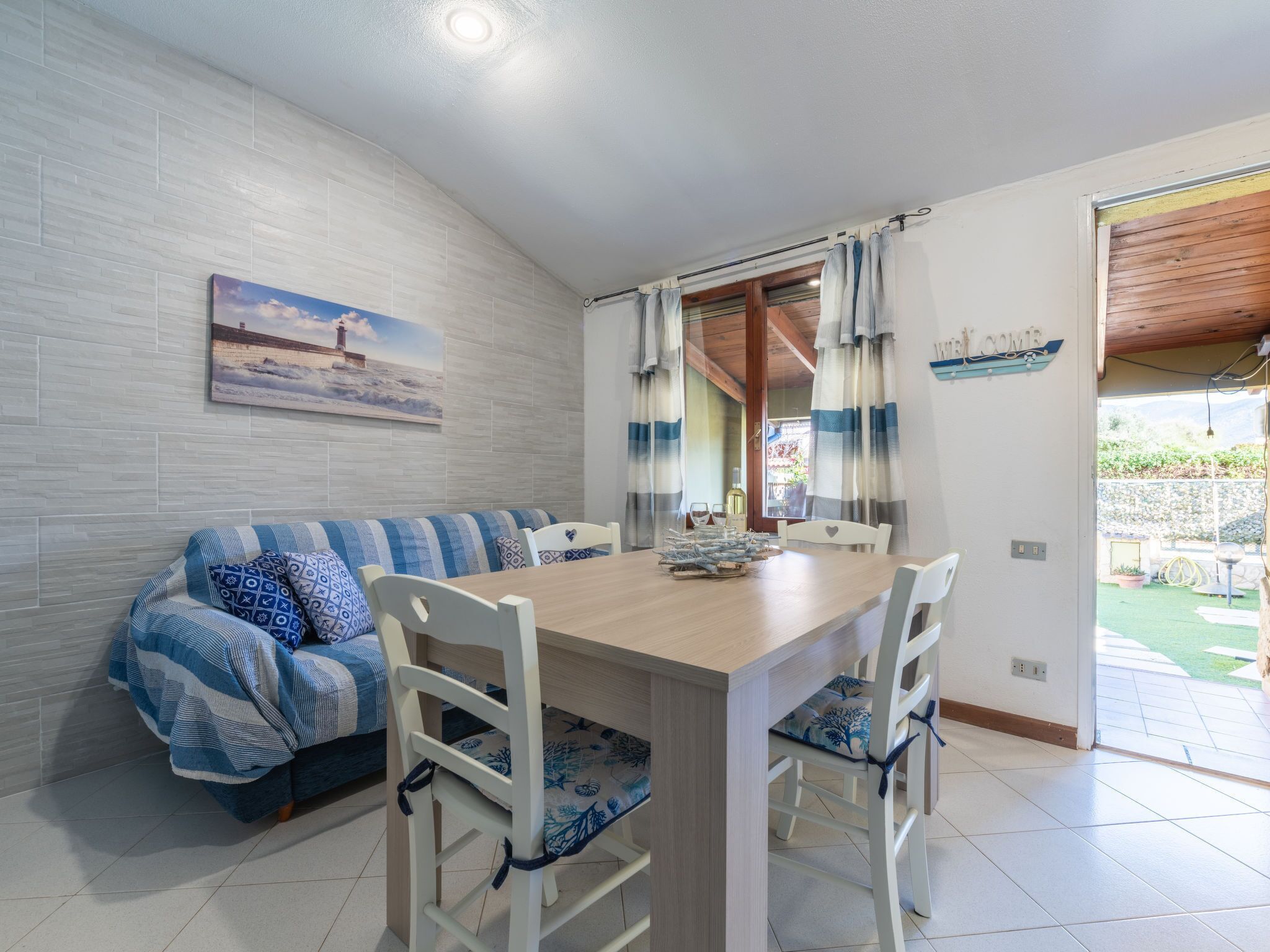 A dining area with a wooden table and white chairs, a blue-striped sofa, and a painting of a lighthouse.