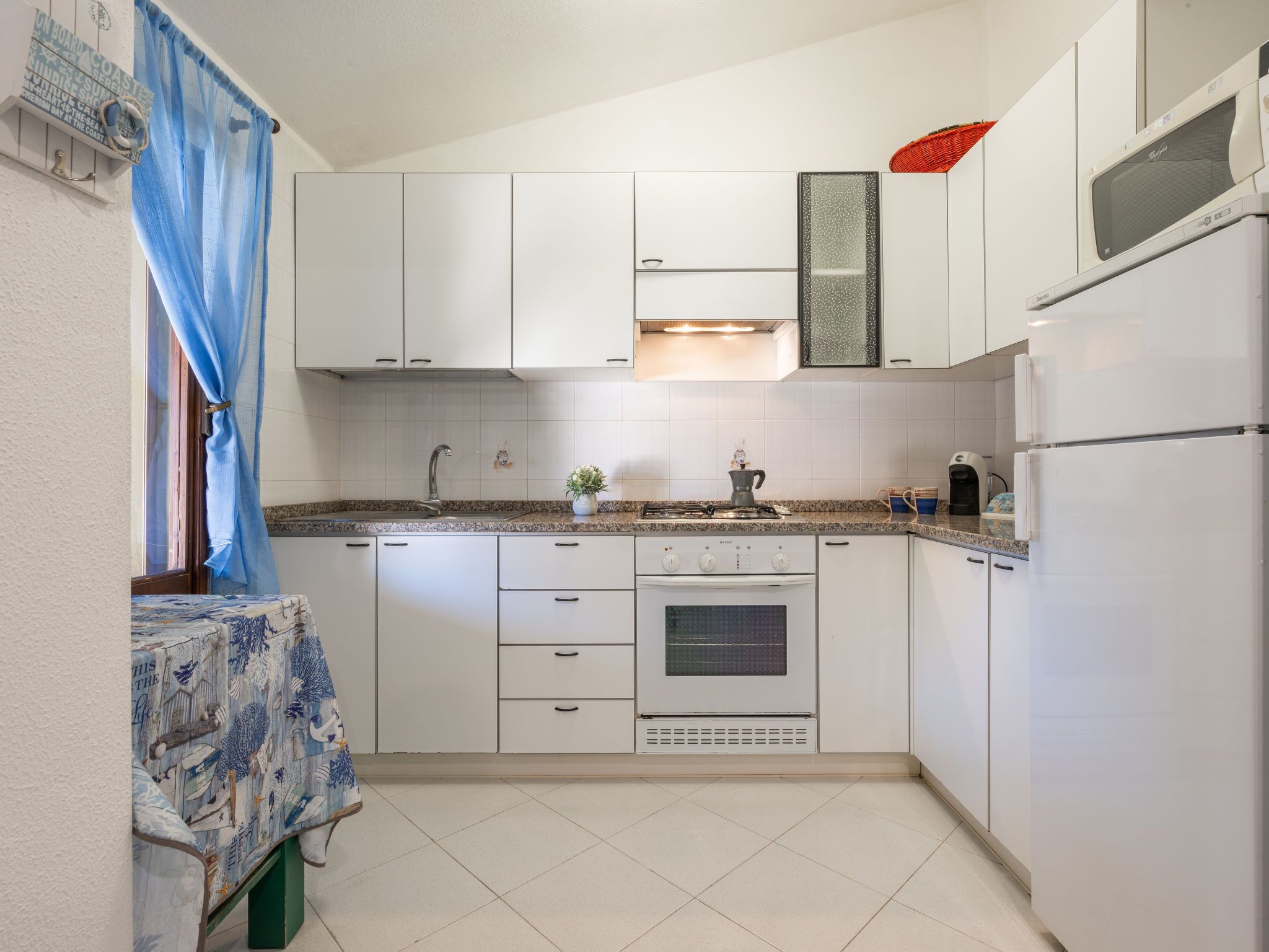 Une cuisine compacte avec des meubles blancs, une cuisinière à gaz, un four encastré et un réfrigérateur.