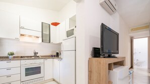 Une cuisine moderne avec des meubles blancs, un four encastré, un réfrigérateur et un meuble TV en bois.