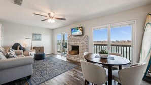 A spacious living room with a fireplace, a dining area, and a balcony with a view. - Sunsets Over Lake Padre | Canal Home | 2 blk to beach (Corpus Christi)