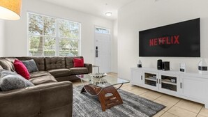 Ein modernes Wohnzimmer mit einer Eckcouch, einem Glastisch und einer weißen Unterhaltungsecke mit einem großen Fernseher, der das Netflix-Logo zeigt.