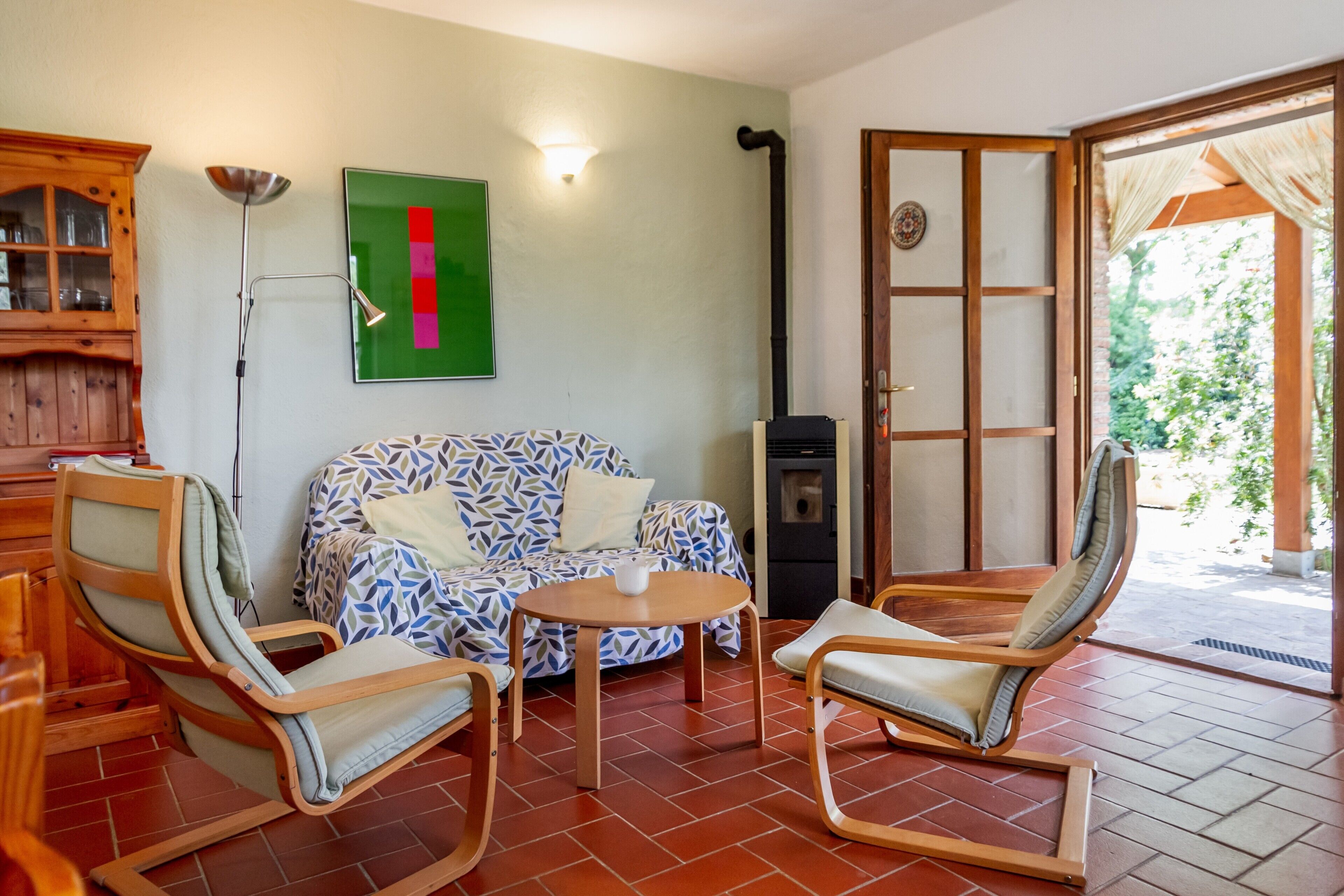 Un salon avec un canapé à motifs, deux chaises en bois, une petite table, un meuble et un mur vert orné d’une bande rouge.