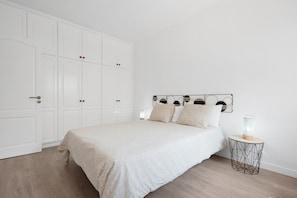 Un dormitorio con cama, armario, mesita de noche con lámpara y aplique de pared.