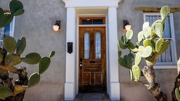 Un edificio con puerta de madera, porche blanco y cactus.