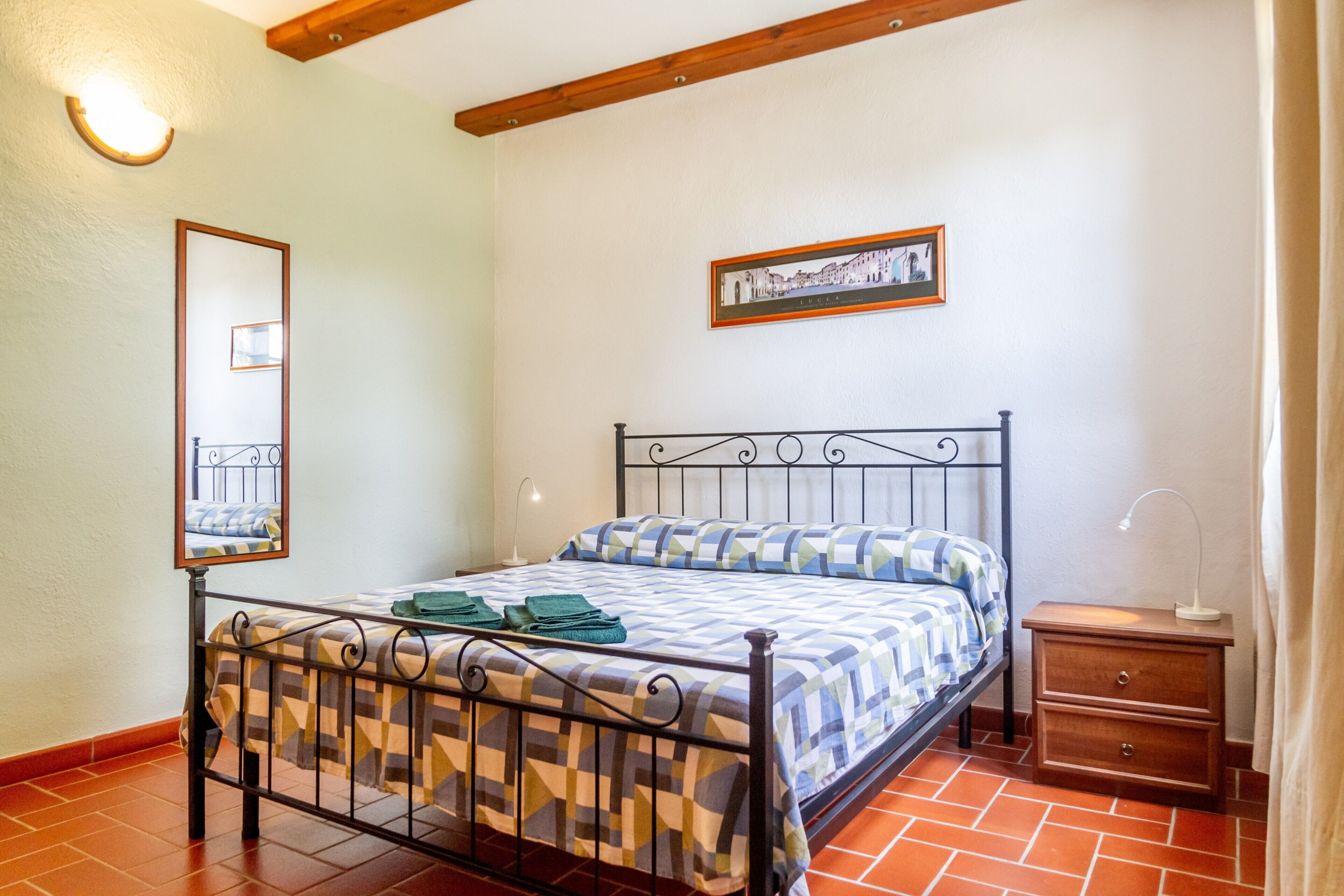 A bedroom with a metal bed frame, a bedside table, a mirror, and a framed picture on the wall.