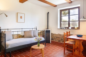 Een kamer met een bed, een tafel met stoelen, een bloevas, een raam en een wandradiator.