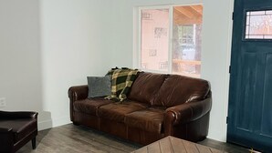 Et værelse med en brun lædersofa, et lille træbord og en blå dør.