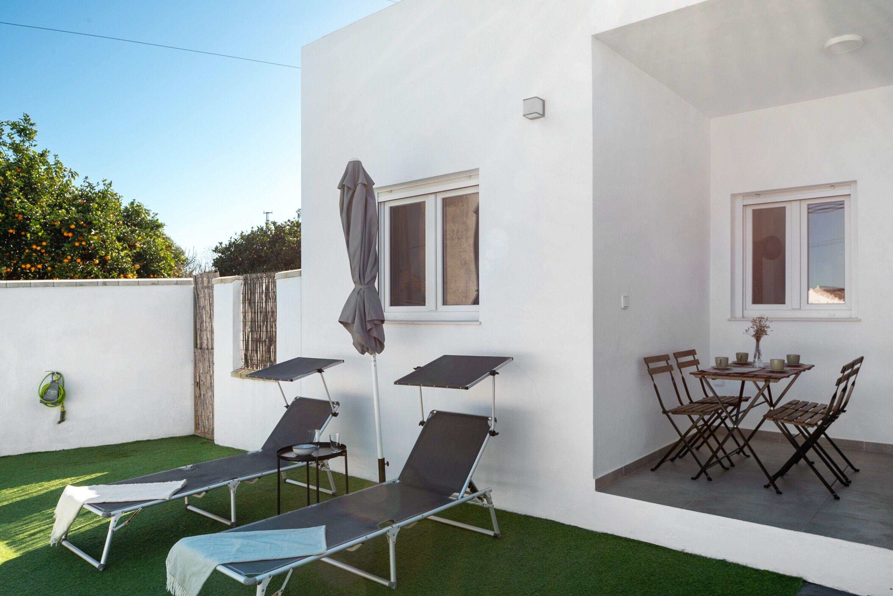 Eine Terrasse mit zwei Liegestühlen, einem Tisch mit Stühlen und einem kleinen Tisch mit einer Vase und Tassen.