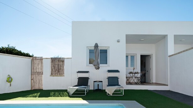 Un área de piscina exterior moderna con dos sillones de descanso, una mesita y un ventanal cubierto.