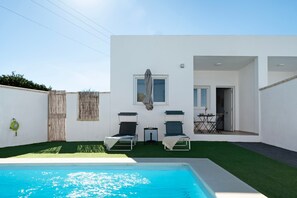 Un espace piscine extérieur moderne, comprenant deux chaises longues, une petite table et une fenêtre protégée.