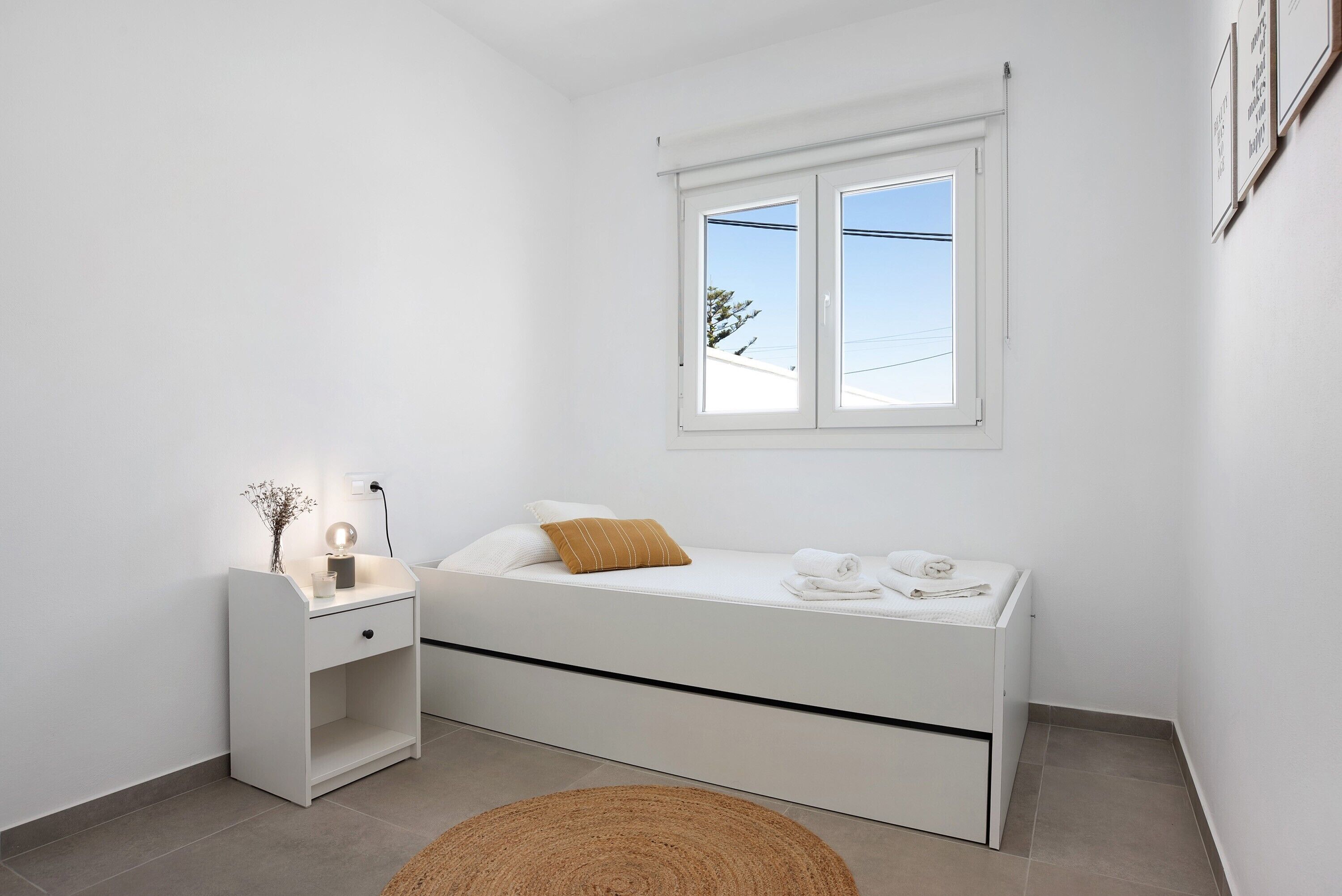 Ein schlicht eingerichtetes Schlafzimmer mit Bett, Nachttisch und Fenster.