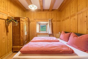 A wooden room with a bed, a radiator, and a window with curtains.
