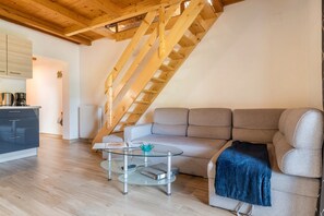 A living room with a sofa, a glass coffee table, a kitchen area with cabinets and appliances, and a wooden staircase. - Apartment "Stofnerhof Neu" with Mountain View, Shared Garden & Wi-Fi (Sarentino)