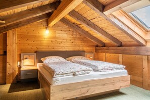 A wooden cabin bedroom with a loft-style ceiling, a bed with floral bedding, a bedside table with a lamp, and a skylight. - Apartment "Stofnerhof Neu" with Mountain View, Shared Garden & Wi-Fi (Sarentino)