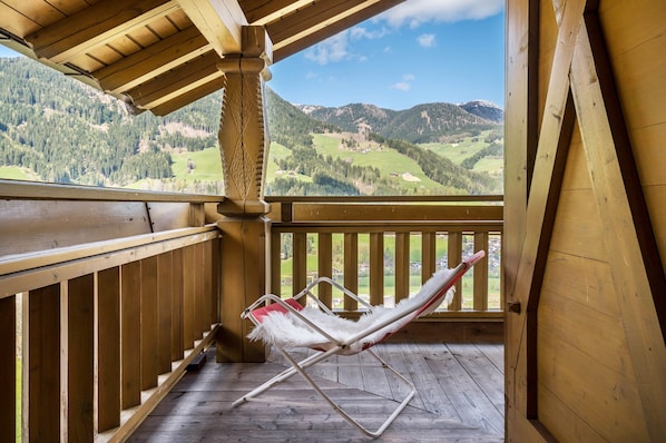 A wooden balcony with a white cushioned chair and a wooden floor.