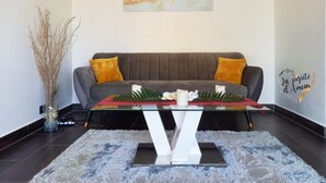 Un salon moderne avec un canapé gris, une table basse en verre et un élément décoratif mural.