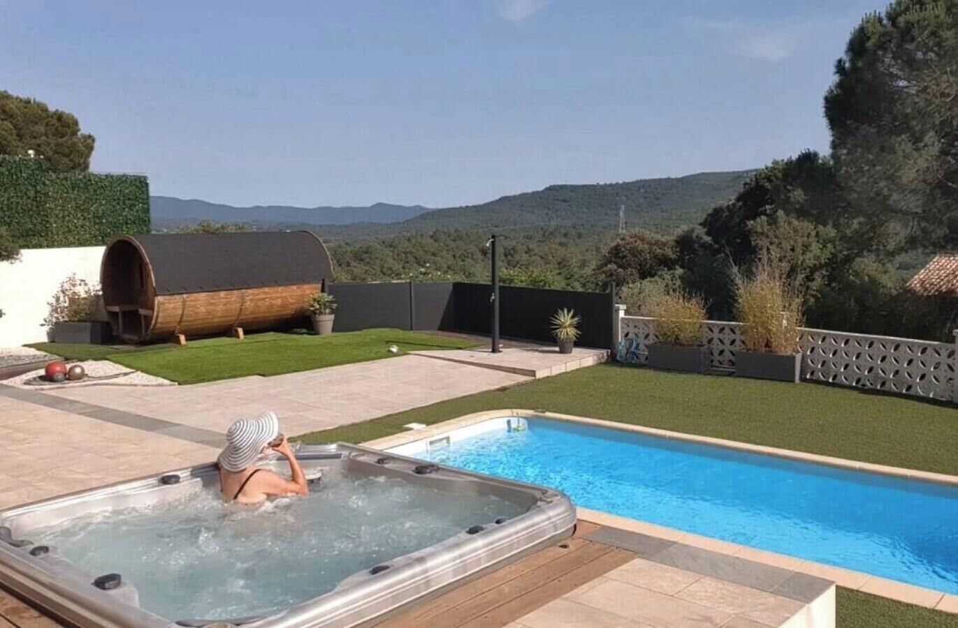Une piscine avec un jacuzzi, une structure en forme de tonneau en bois et une vue sur les collines.