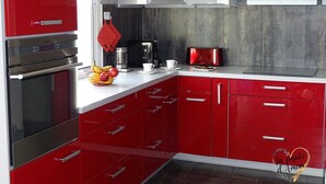 Une cuisine moderne avec des meubles rouges, des appareils en acier inoxydable et un plan de travail blanc.