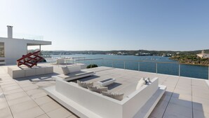 Une terrasse moderne sur le toit, au design minimaliste, comprenant un espace salon avec des coussins et une sculpture géométrique rouge.