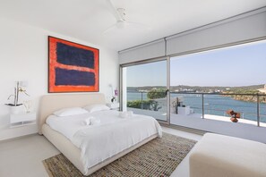 Un dormitorio moderno con una cama grande, vista al mar y un balcón con barandilla.