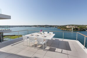 Une terrasse avec une table dressée pour le dîner, offrant une vue sur une étendue d’eau, avec, au loin, des terres et des bâtiments.